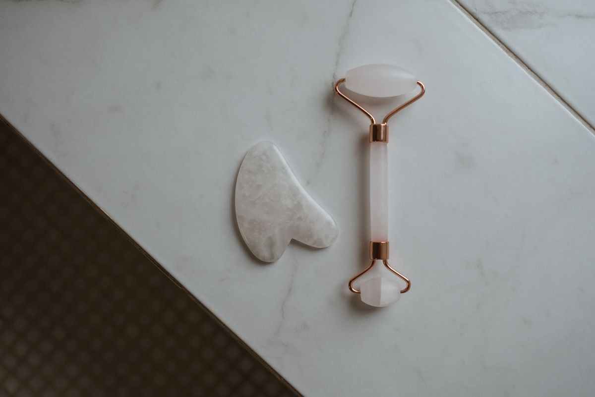 Gua sha stone and facial roller on a marble surface
